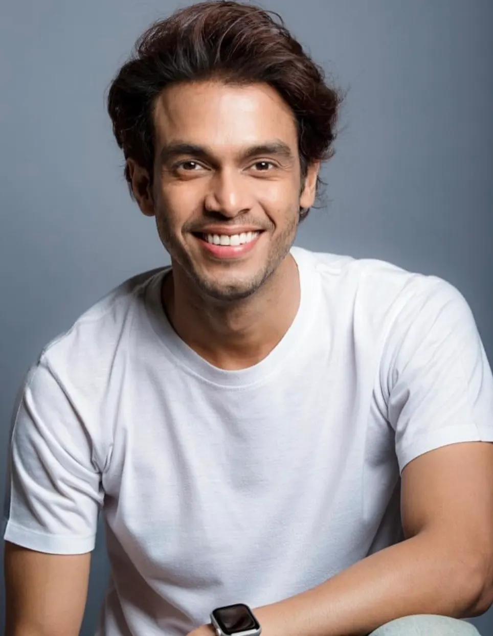 Varun Patel smiling in a white T-shirt against a grey studio backdrop