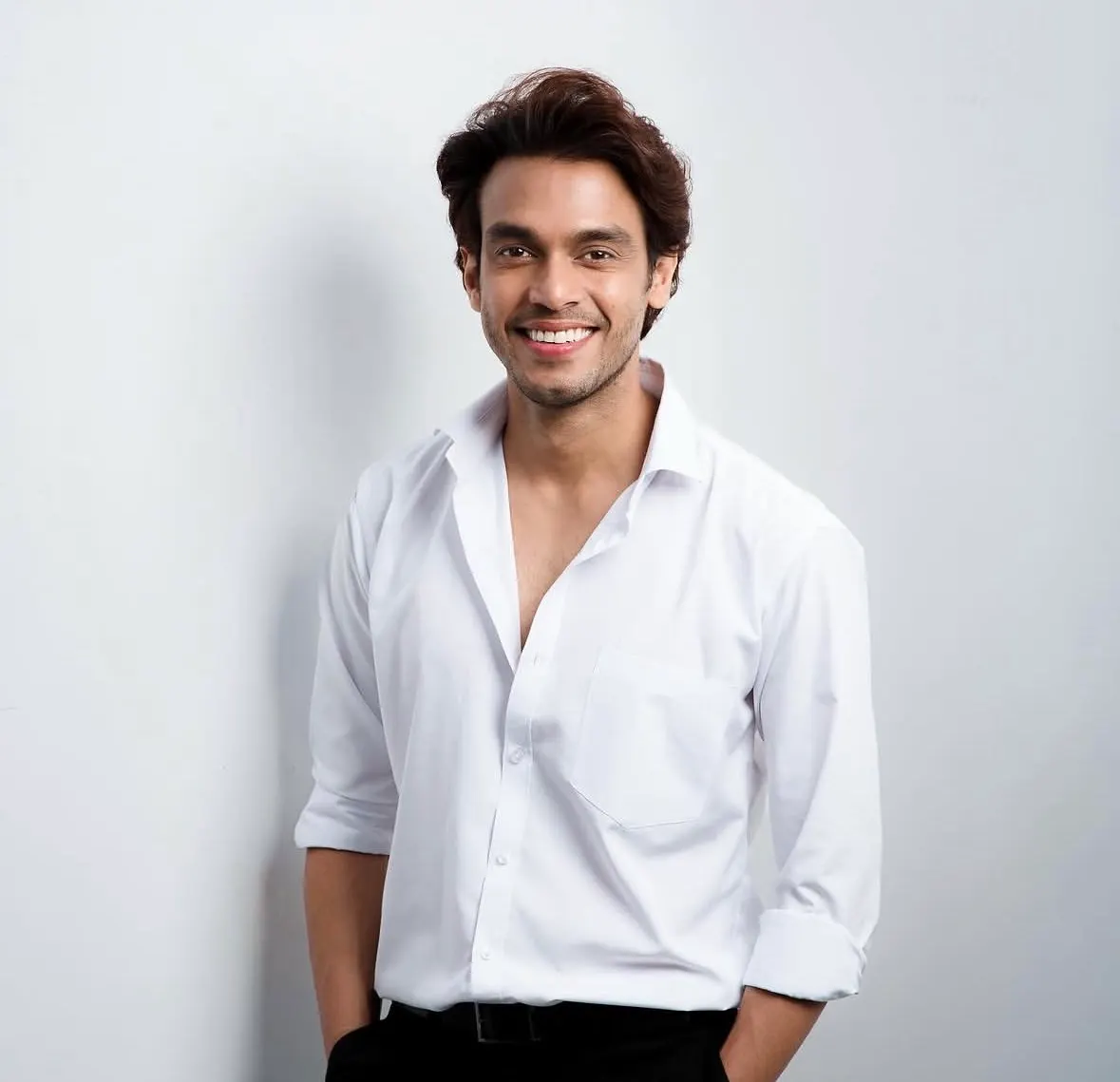 Varun Patel in a white shirt, smiling, leaning against a white wall