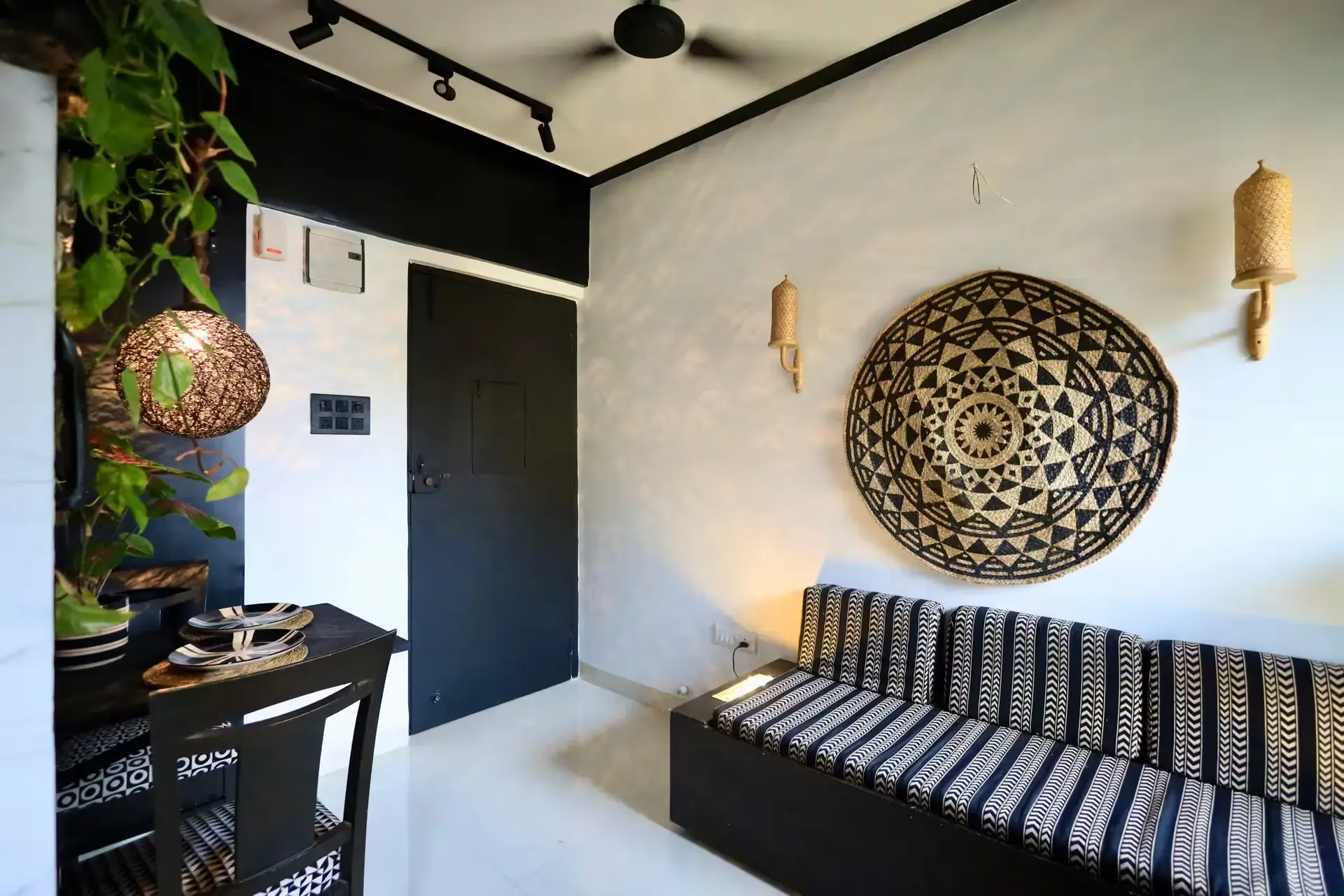 Black-and-white striped daybed beneath a woven basket wall piece and brass wall lamps