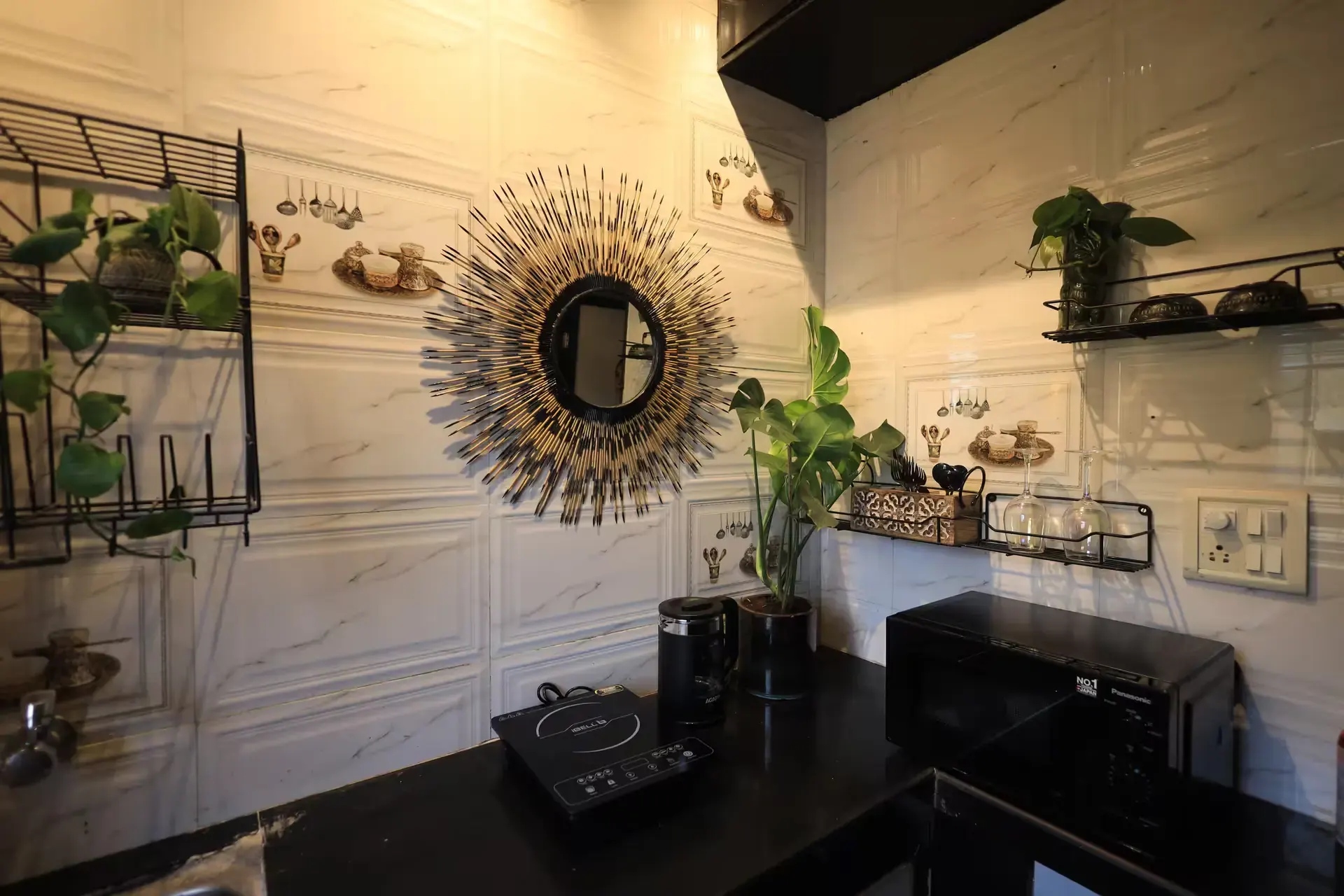Kitchen with a sunburst mirror, trailing plants and an induction hob on a black counter