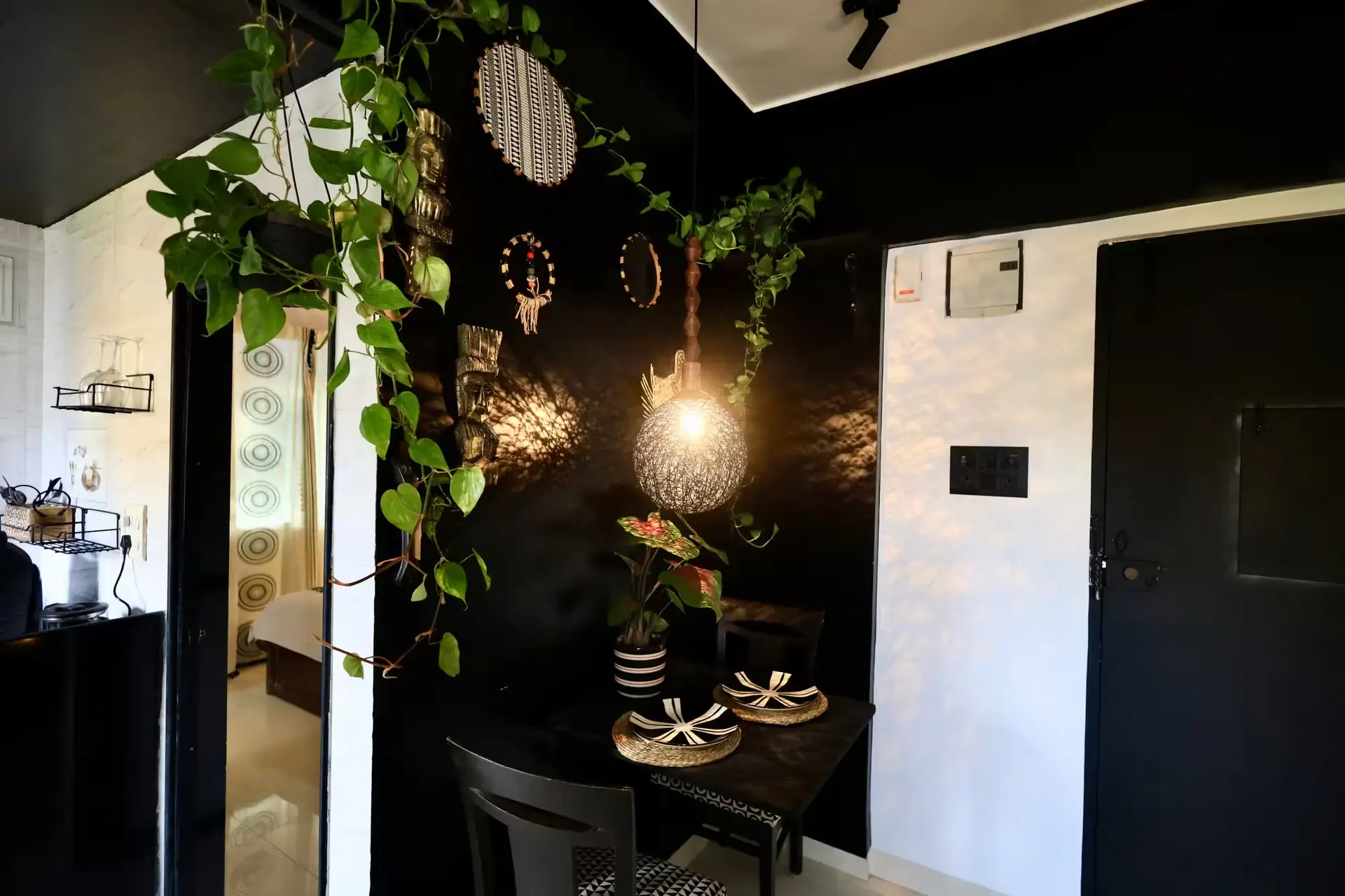 Dining nook with a round pendant lamp and trailing plants against a black wall