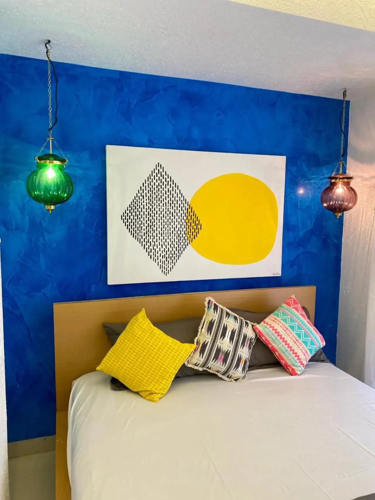 Bedroom with a deep blue wall, a geometric artwork and bright cushions