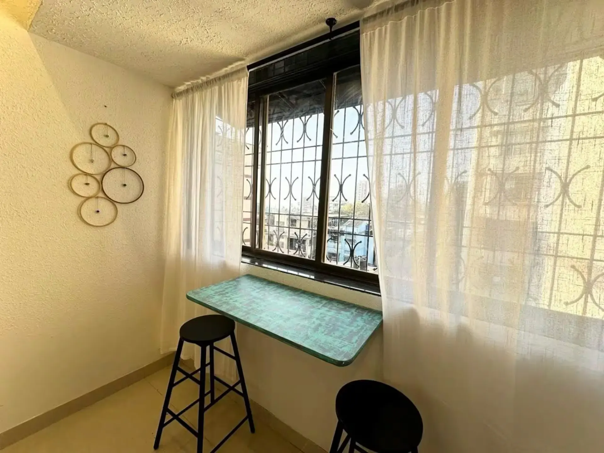 Window workspace with a teal counter, black stools and white curtains