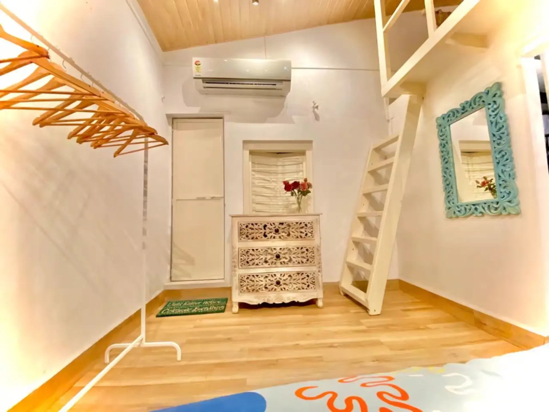 Entry with a ladder up to the loft, a carved white chest and a turquoise mirror