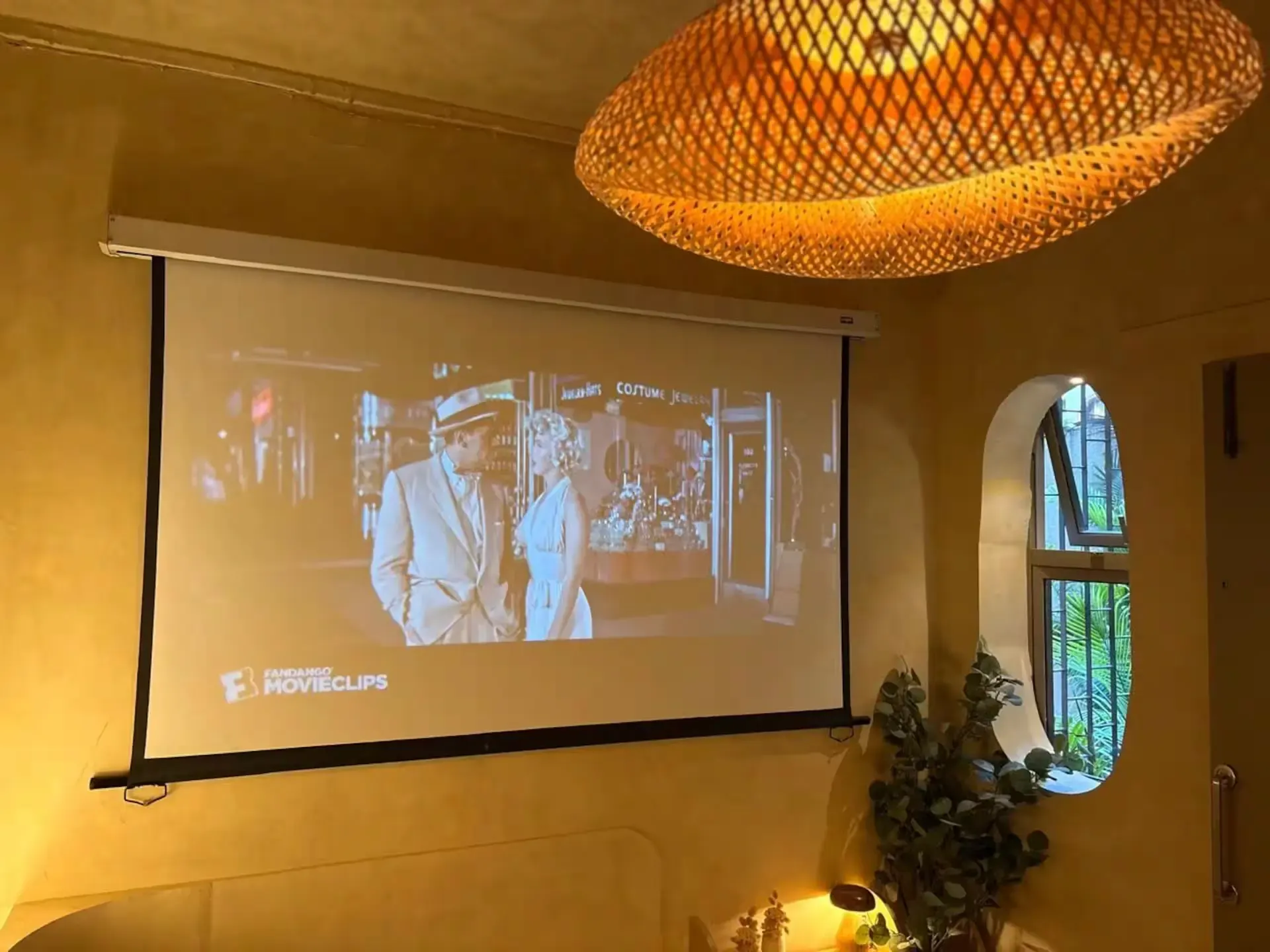 Projector screen playing a film beneath a woven bamboo pendant light