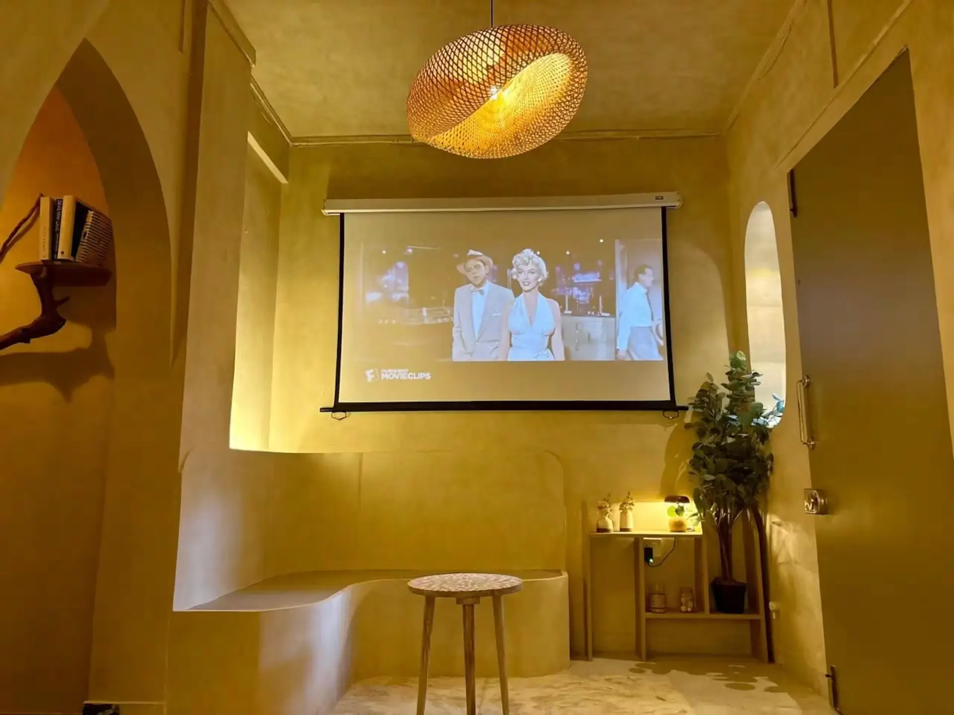Arched living room with a projector screen, a woven pendant light and a round stool