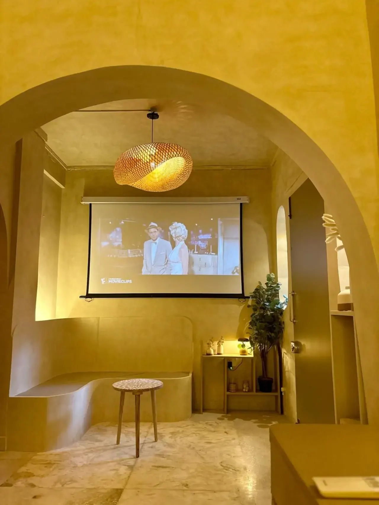 A rounded arch framing the projector screen and a small stool in warm ochre plaster