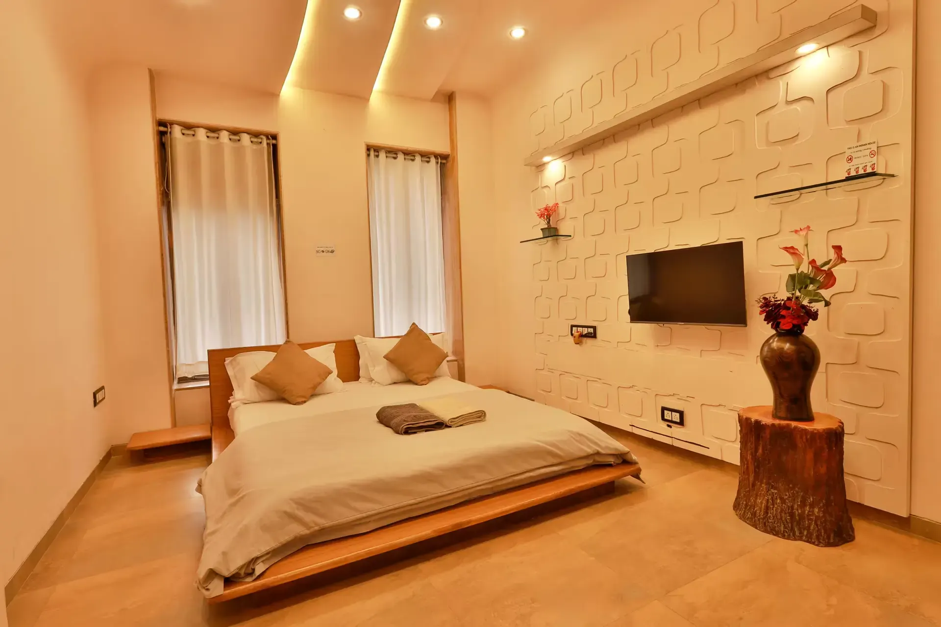 Bedroom with a low platform bed, a wall-mounted TV and a tree-stump side table