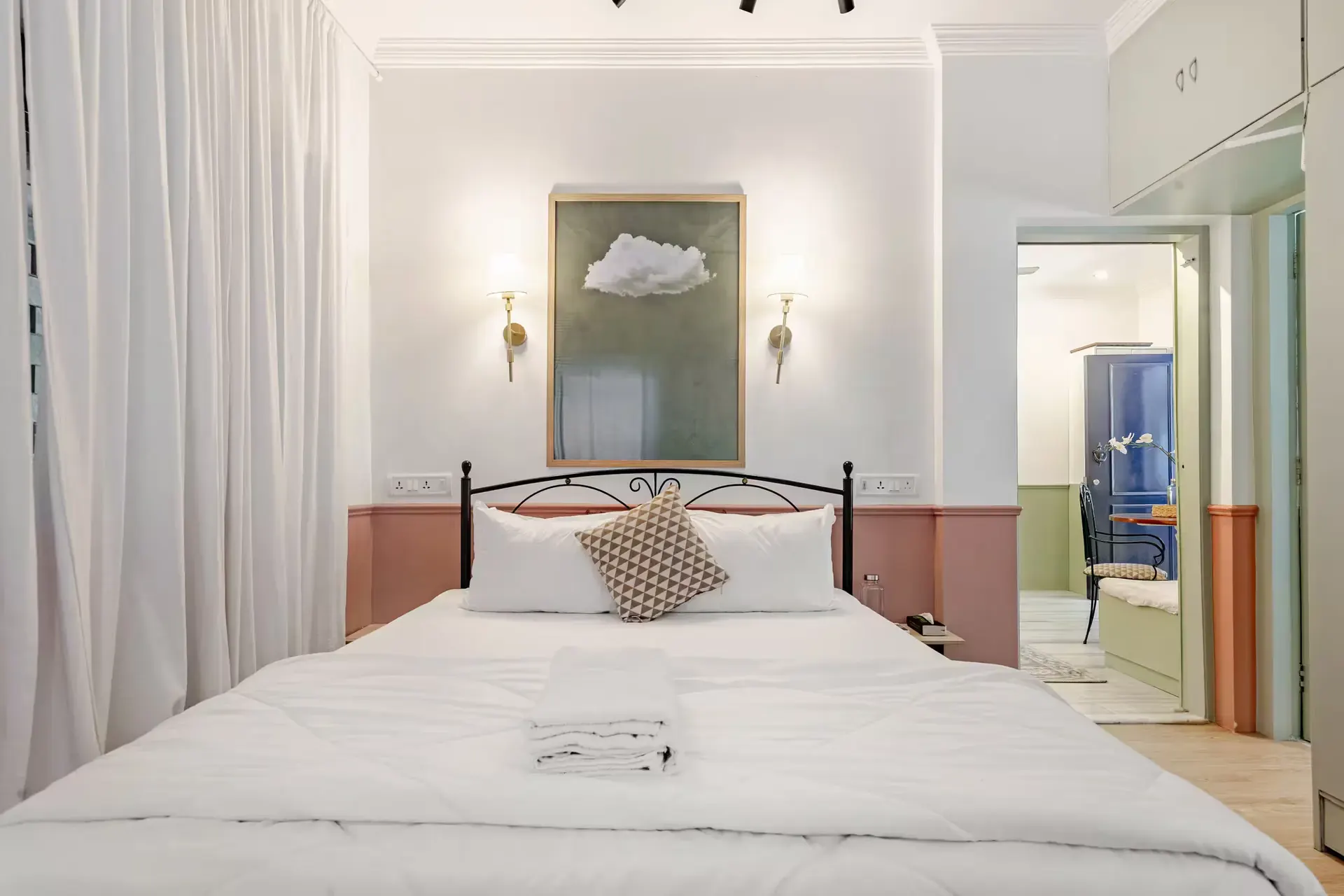 Bedroom with a white-linen double bed under a framed cloud artwork and brass wall lights