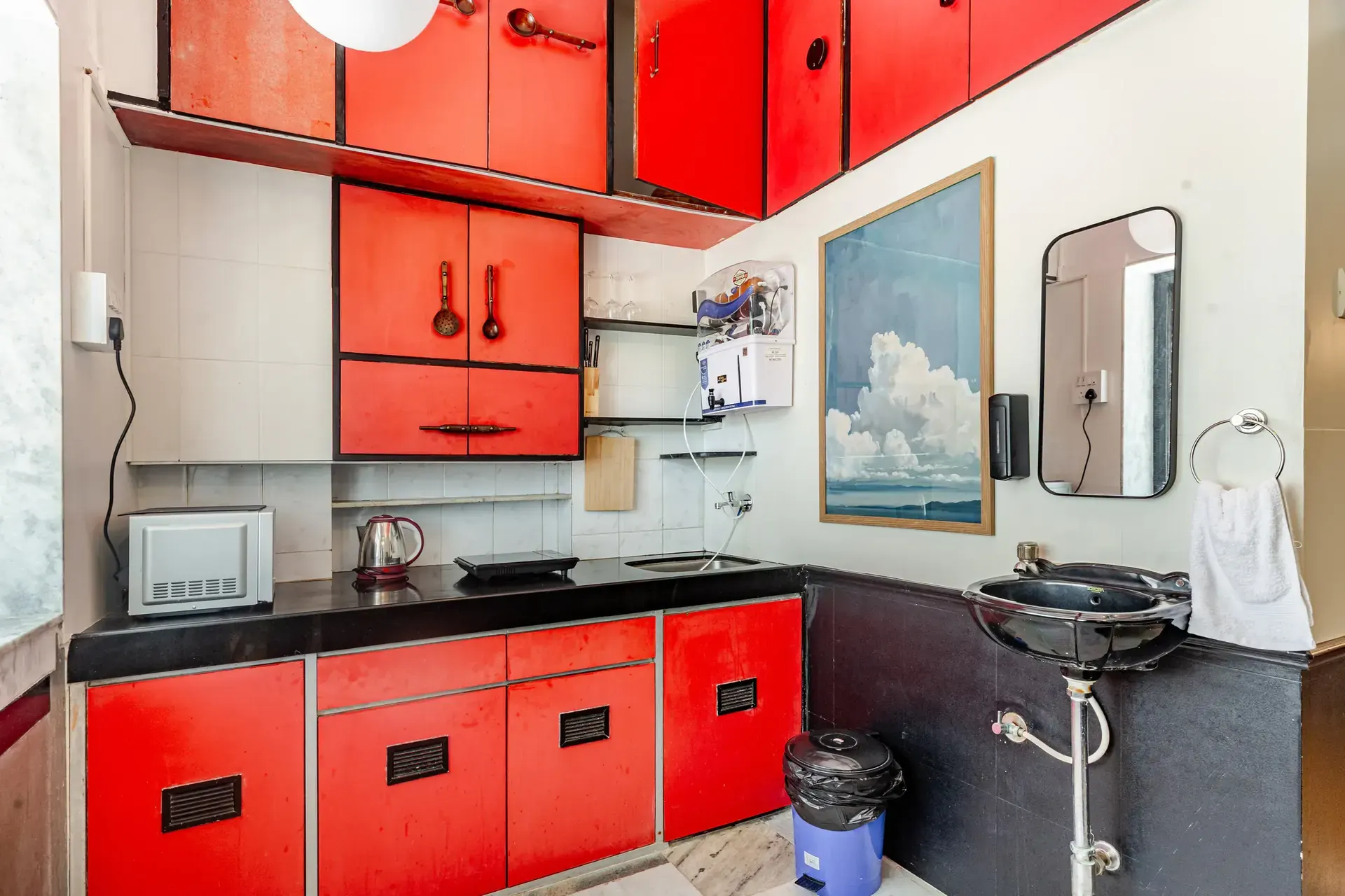 Kitchenette with red cabinetry, a black wash basin and a framed cloud painting