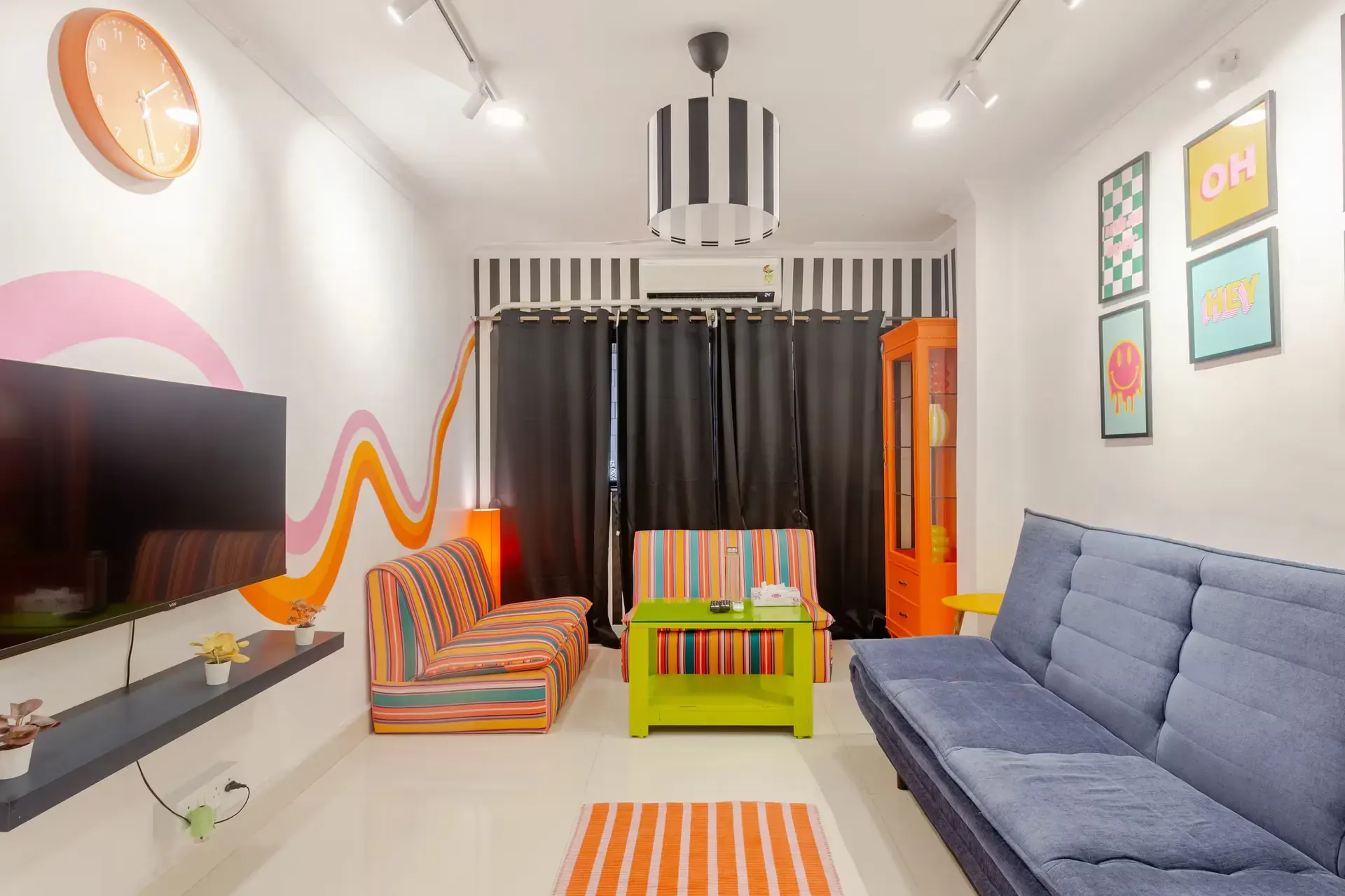 Living room with striped armchairs, a navy sofa bed, a lime-green table and framed pop prints