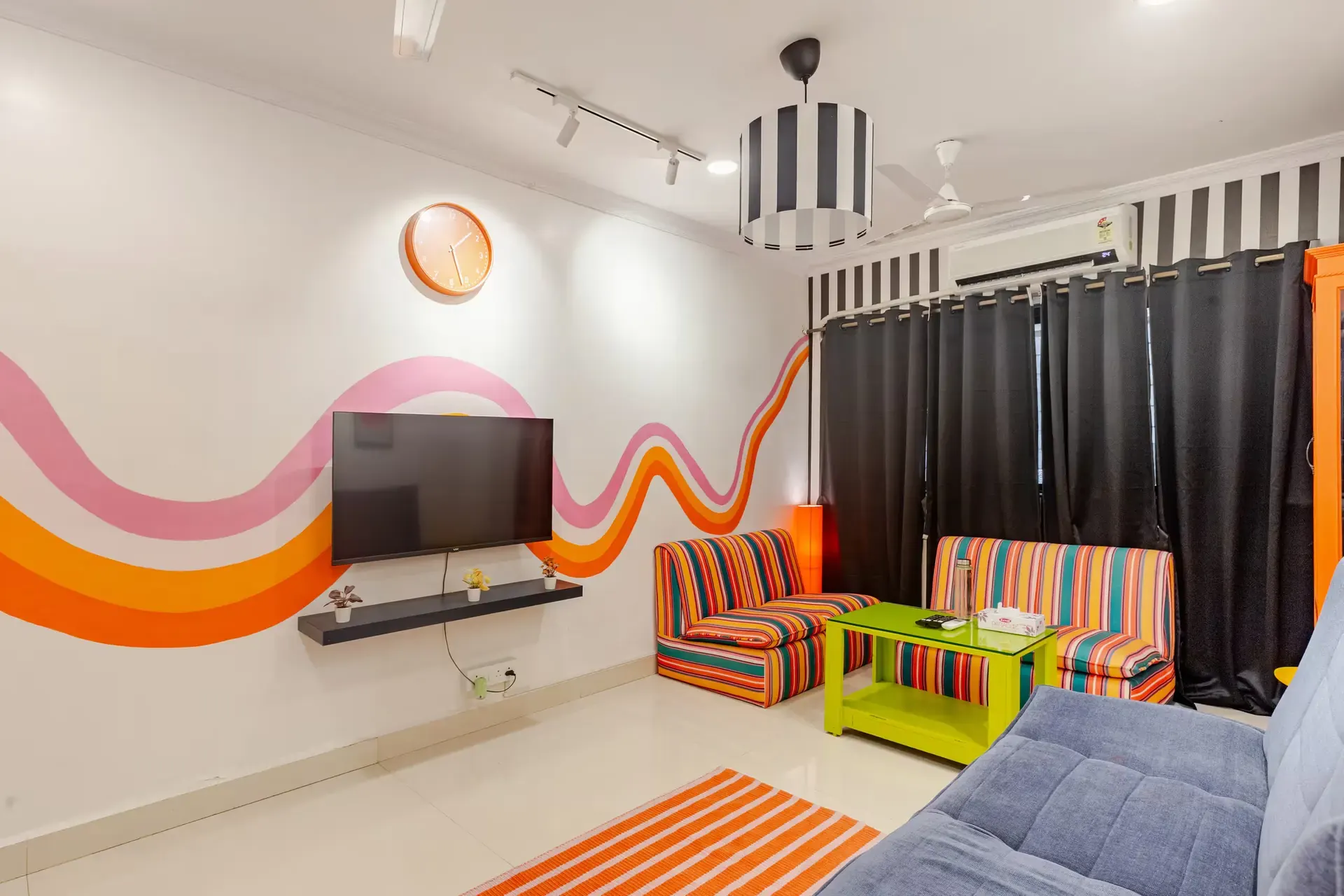 Orange and pink wave painted on the wall beside the TV, above striped seating