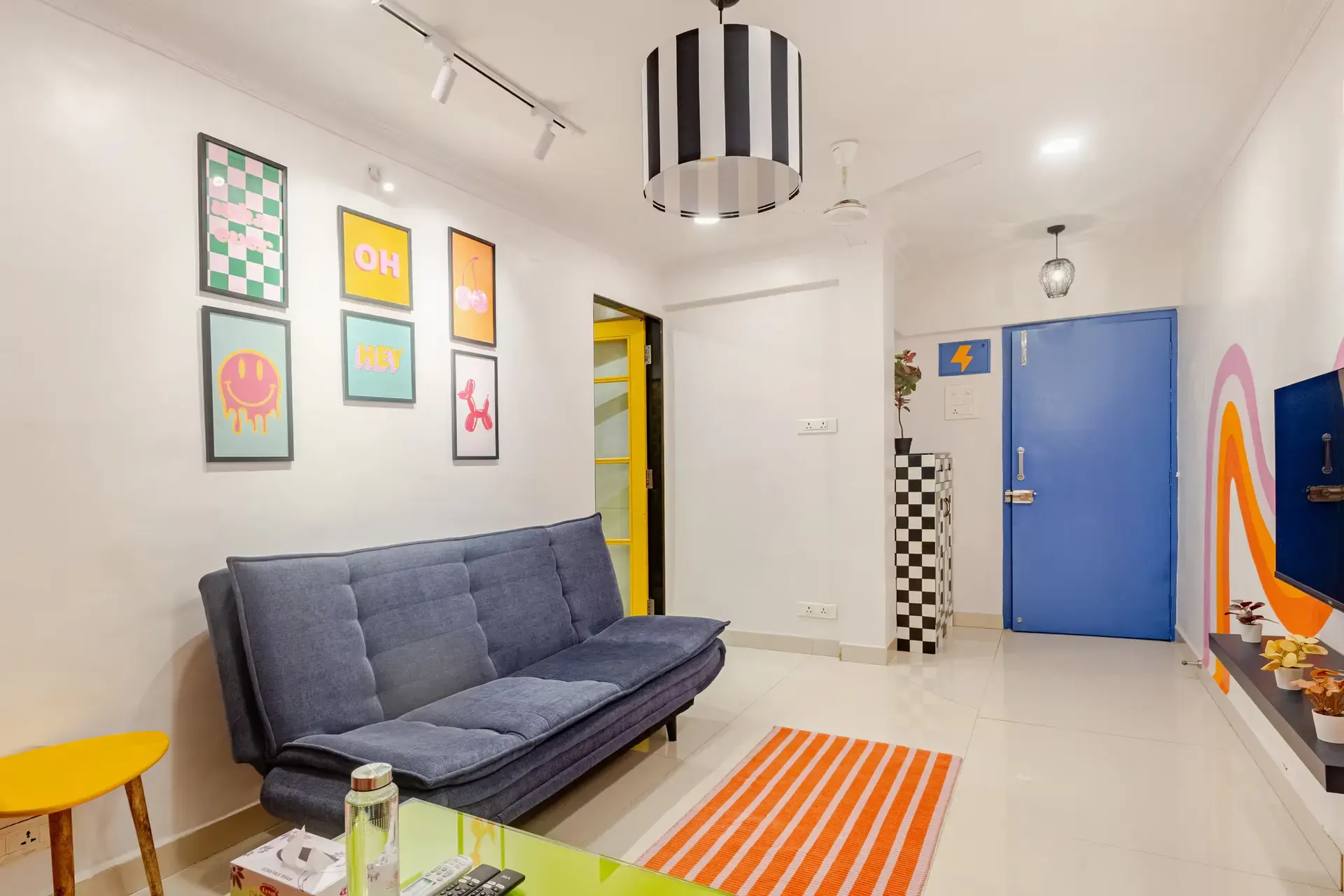 Sofa bed beneath a gallery of colourful framed prints, beside a bright blue door
