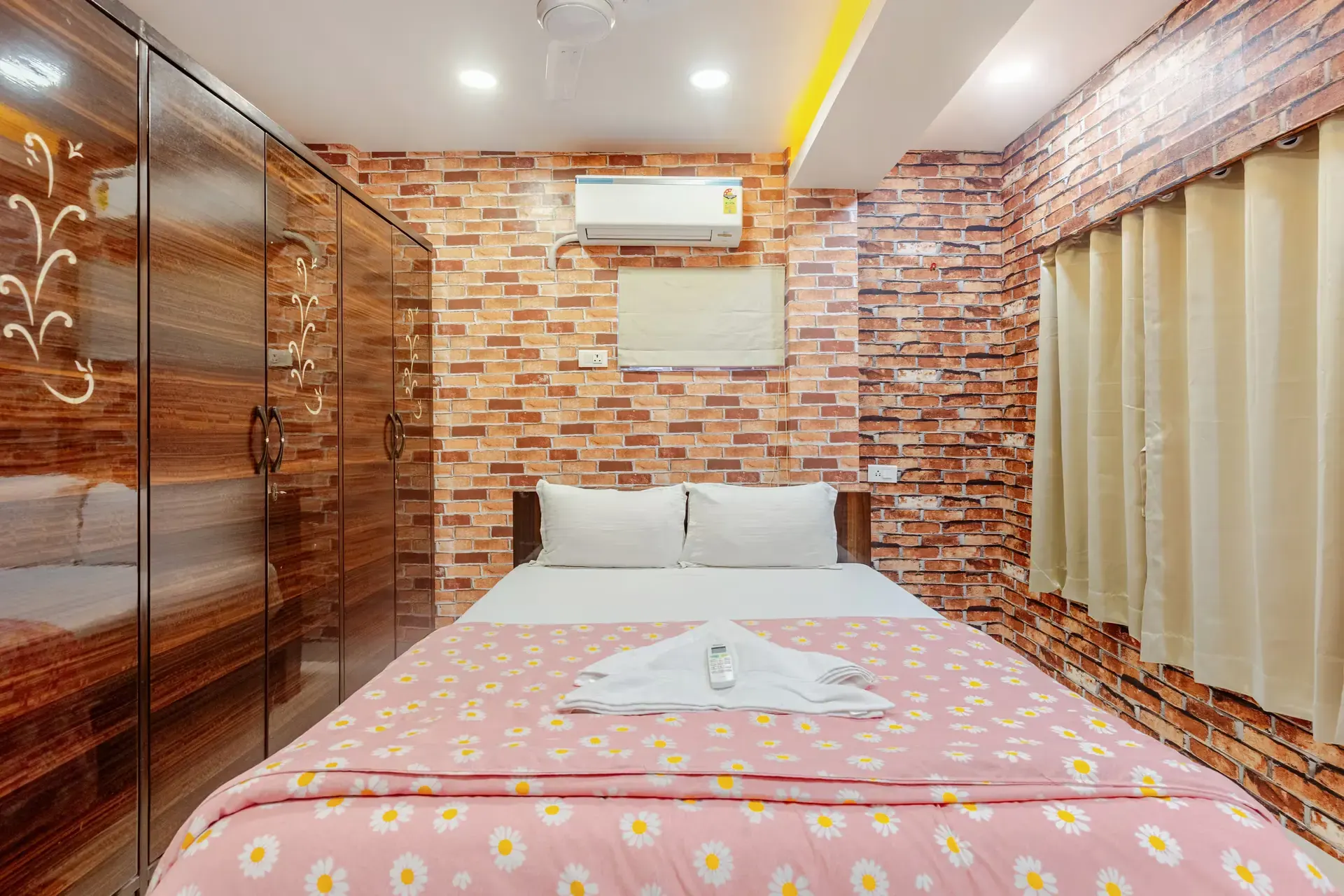 Double bed with a pink floral throw, in front of a brick-effect wall and a wooden wardrobe