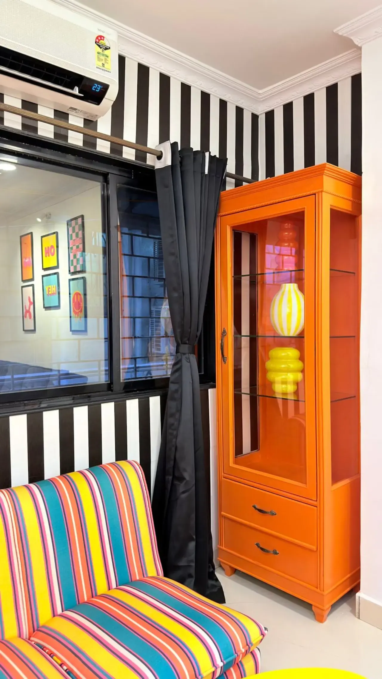 Black-and-white striped wall with an orange display cabinet and a striped seat