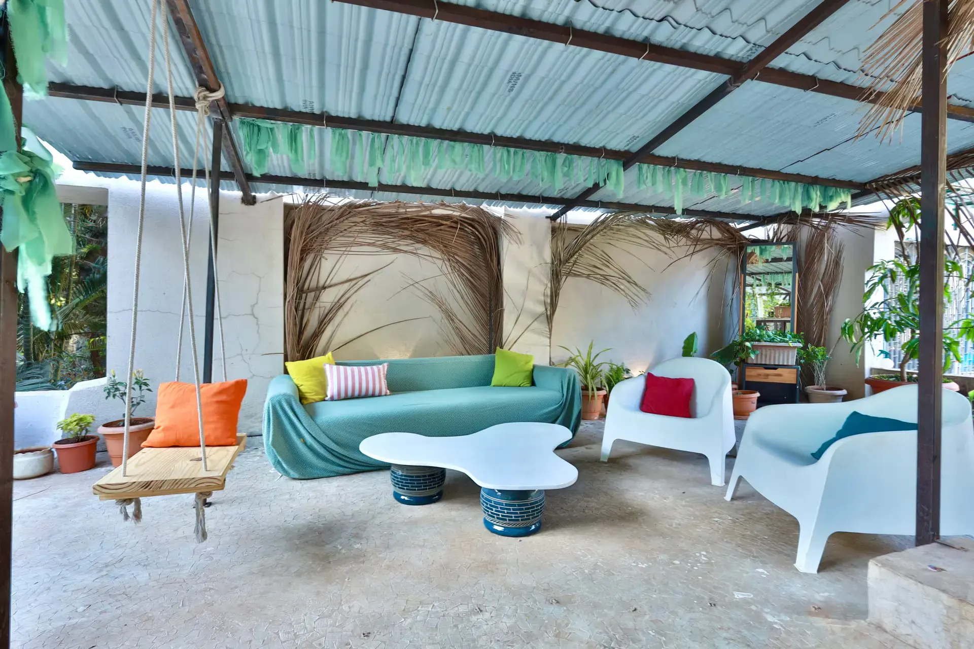 Covered terrace with a teal sofa, a wooden swing and a cloud-shaped coffee table