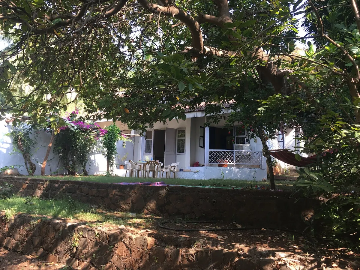 Kashid Cottage's white exterior seen through garden trees