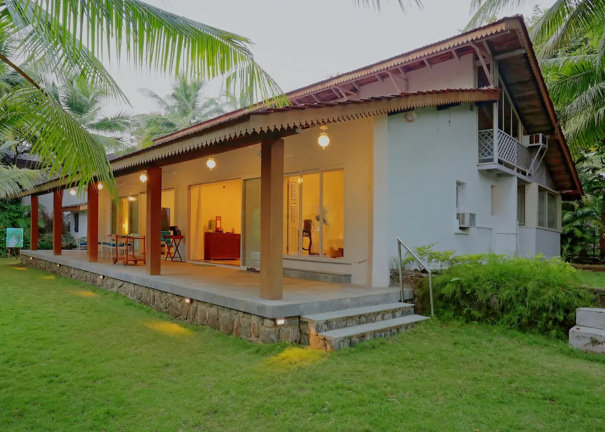La Mer's lit veranda and Konkan-style tiled roof at dusk, framed by palm trees
