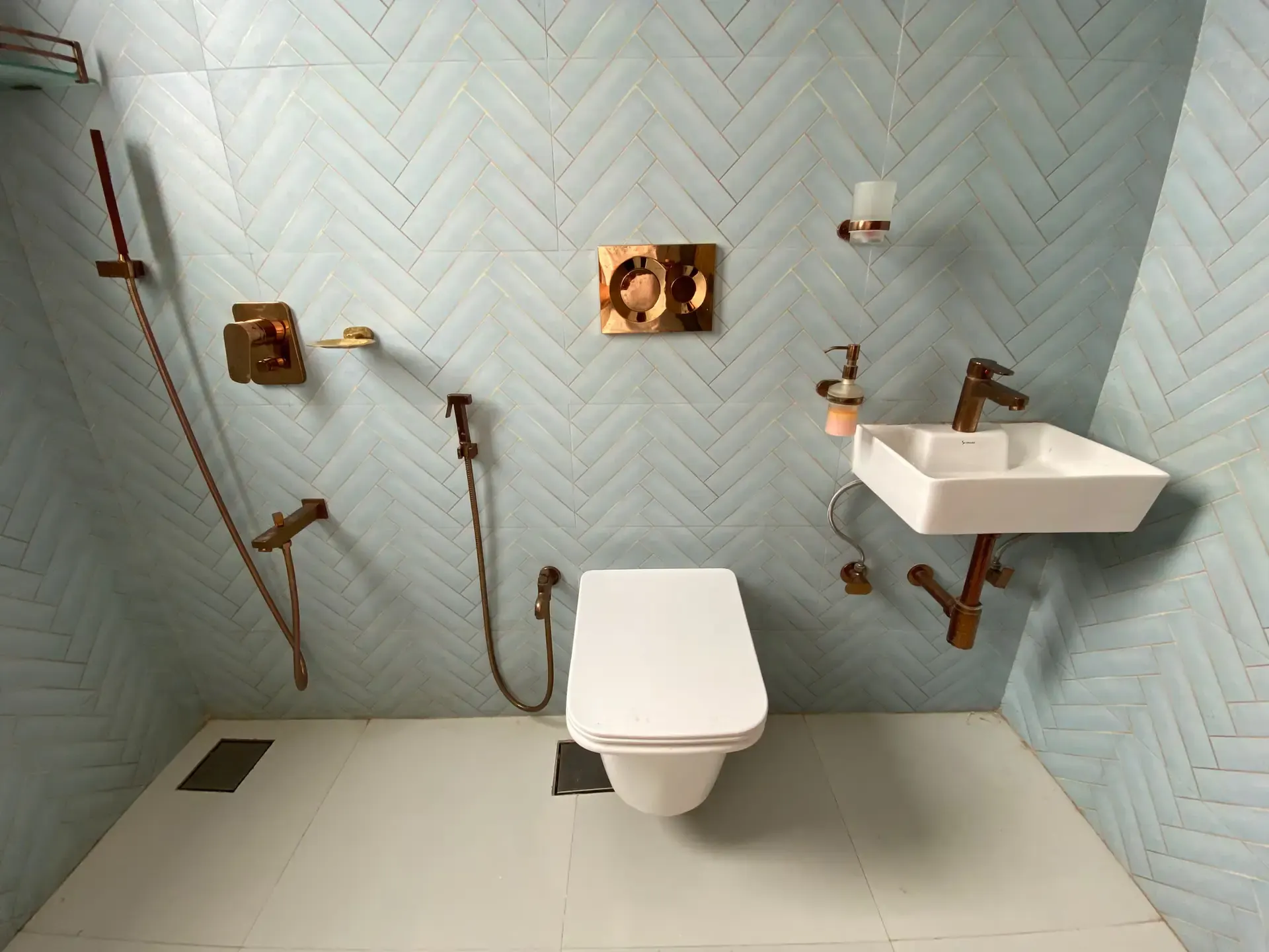Bathroom with pale blue herringbone tiles and copper-toned fittings