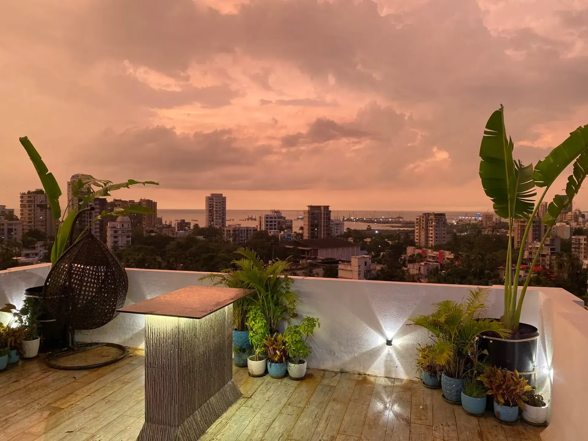 Terrace at dusk under a pink sky, with a hanging chair and a view over the city